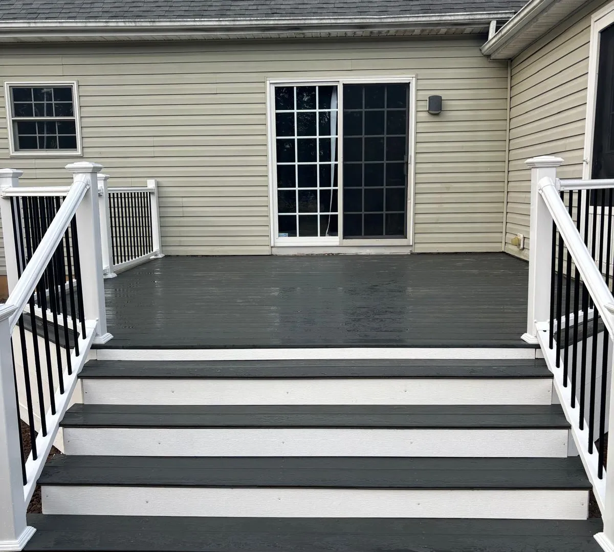 Composite deck entrance with white railings, black balusters and wide stairs by Community Fence & Deck Builders